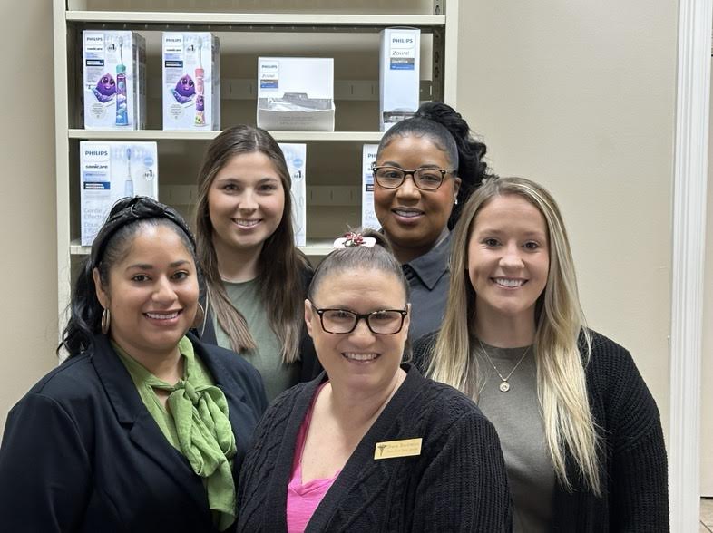 Four smiling women stand in front of shelves.